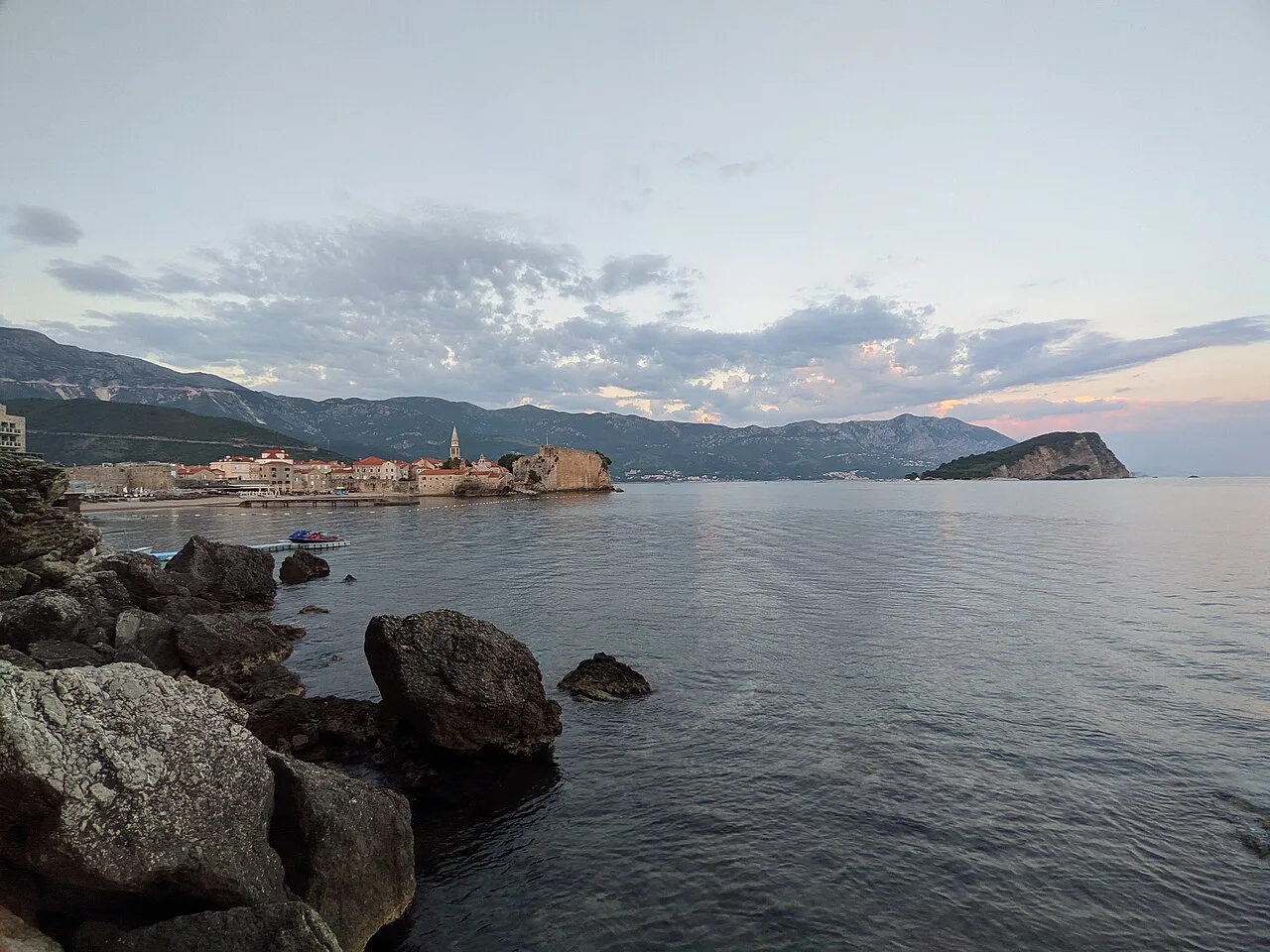 Budva Old Town seen across the bay from the rocky shore.