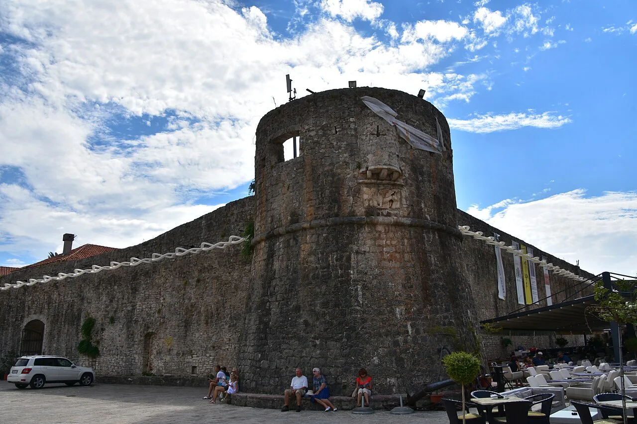 A tower of Budva's old town walls with café tables below.