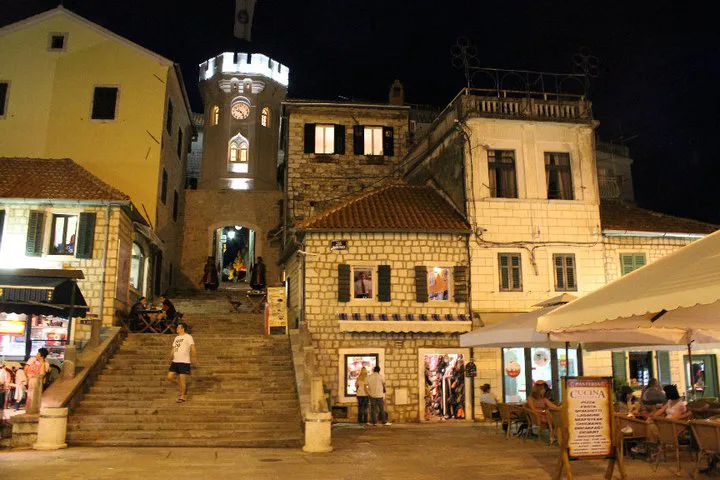 Herceg Novi's main square and clock tower lit up at night.