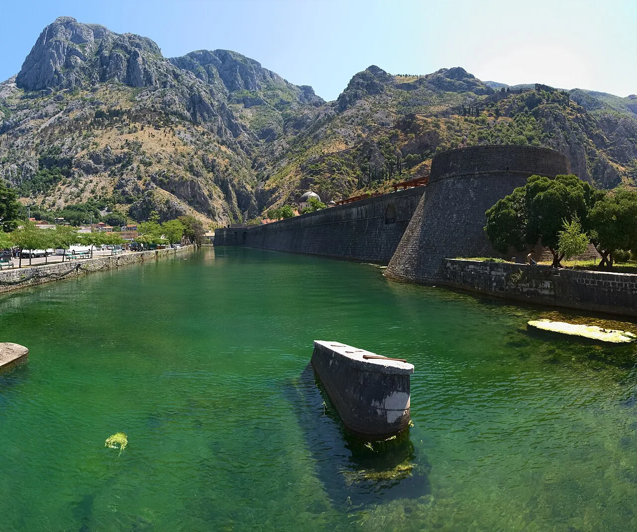 Kotor's city walls rising above the moat, with mountains behind.