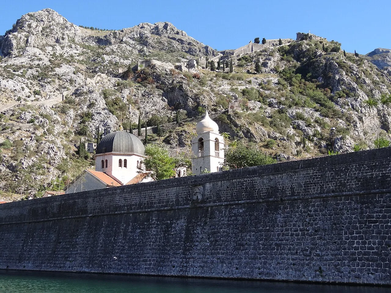 Kotor's old town wall with churches on the slope behind.